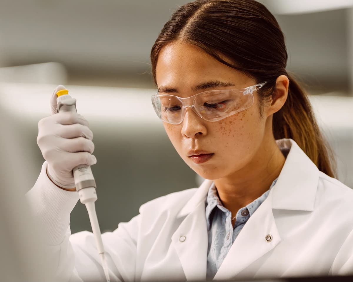 Close up image of a female holding a single pipette in one hand, and looking down.